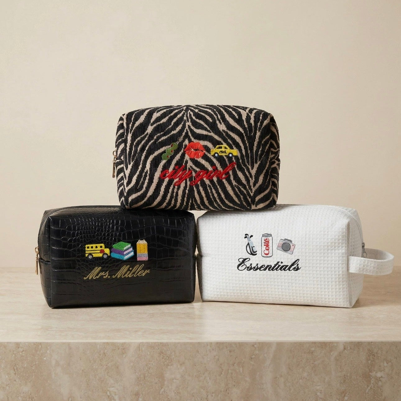 Three cosmetic bags with embroidered designs on a beige surface
