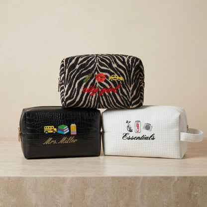 Three cosmetic bags with embroidered designs on a beige surface