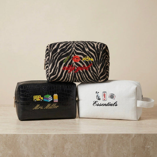 Three cosmetic bags with embroidered designs on a beige surface